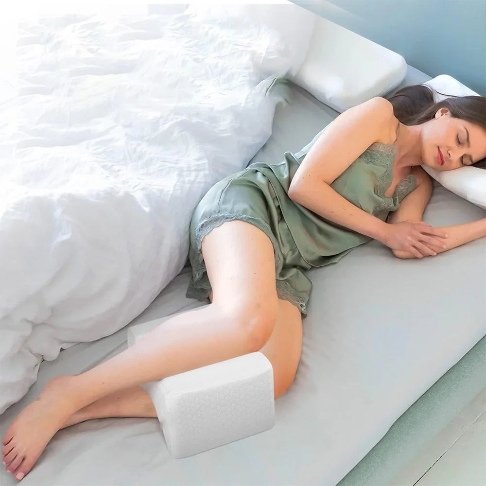 Femme dormant sur le côté avec un coussin genoux blanc en mousse placé entre les jambes ; housse texturée visible.