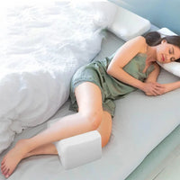 Femme dormant sur le côté avec un coussin genoux blanc en mousse placé entre les jambes ; housse texturée visible.