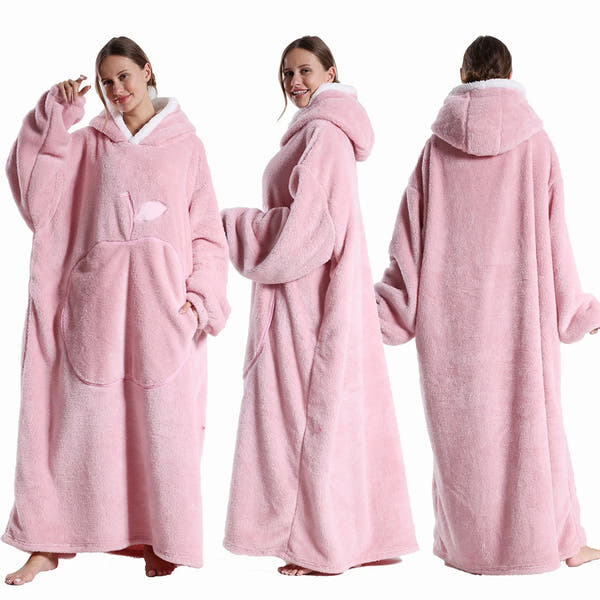 Deux vues d’une couverture-hoodie oversize rose en sherpa portée par une femme ; capuche doublée blanche et grande poche kangourou visible.
