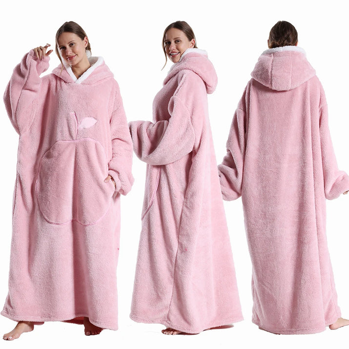 Deux vues d’une couverture-hoodie oversize rose en sherpa portée par une femme ; capuche doublée blanche et grande poche kangourou visible.